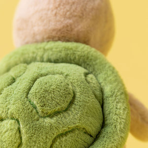Green plush toy held by a hand against a yellow background