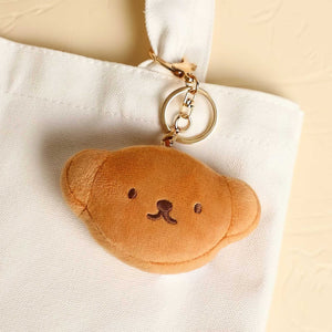 Brown teddy bear-shaped keychain on a white bag with a beige background