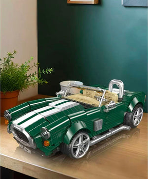 Model of a green convertible car on a wooden surface with a plant in the background.