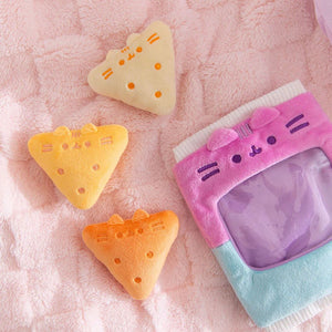 Three triangular yellow and orange cat-shaped items on a pink textured surface with a pink and blue pouch.