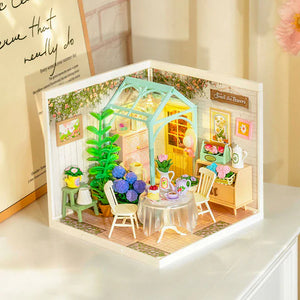 Miniature model of a garden scene with a table, chairs, and plants inside a framed display.