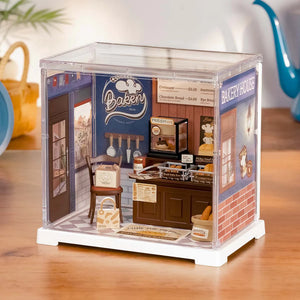 Model bakery display case with miniature furniture and decor on a wooden surface.
