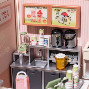Miniature bubble tea shop setup with signs, cups, and kitchenware on a pink wall.