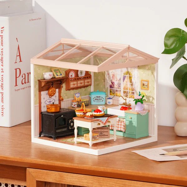 Miniature dollhouse kitchen set on a wooden surface with a book and plant in the background.