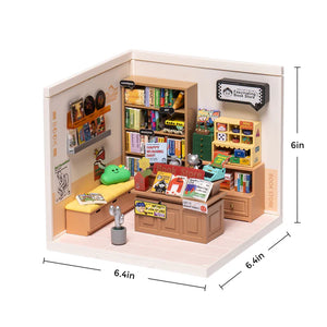 Miniature model of a room with furniture and items, including a bookshelf and desk, with dimensions indicated.