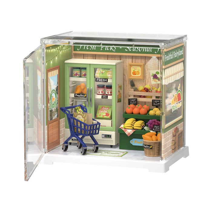 Model of a grocery store with a shopping cart in front on a white background