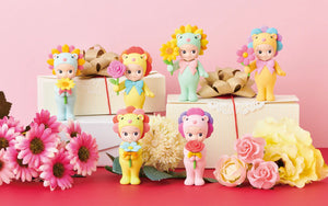 Toy figures with colorful hair and accessories on a pink background with flowers and gift boxes.