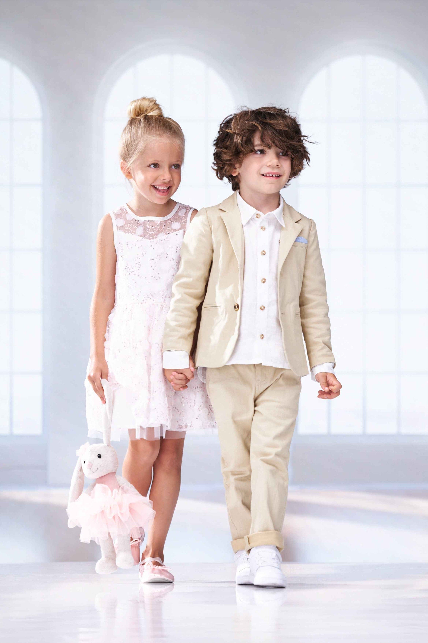 Two children in formal attire standing in a bright, minimalistic room.