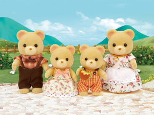 Four teddy bear toys in a scenic outdoor setting with mountains and greenery.