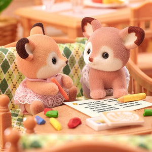 Two plush deer toys sitting at a table with crayons and paper.