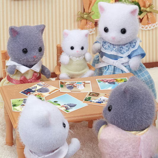 Plush toy cats sitting around a table with pictures on a decorative background
