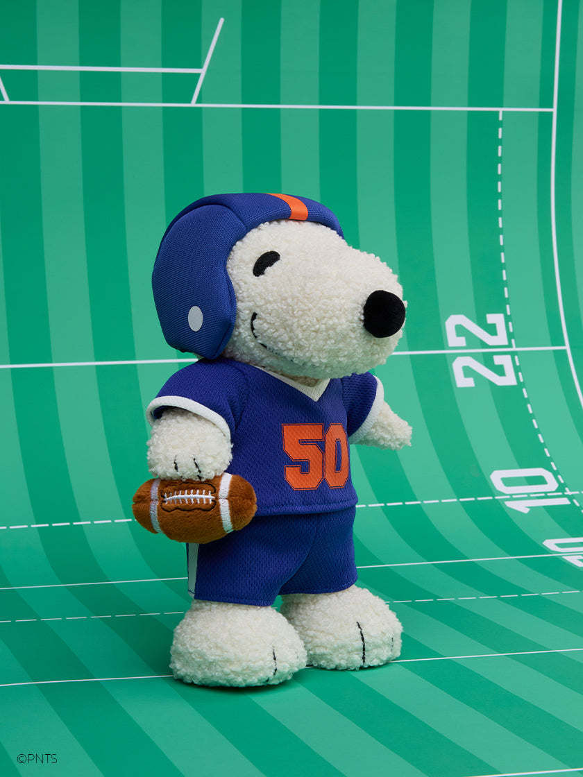 Bon Ton Toys Peanuts American Football Snoopy dressed in sporty outfit with football on a green field backdrop.