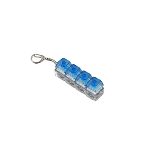 A small keychain charm featuring four translucent blue LEGO-style bricks attached to a silver split ring, shown on a plain gray background.