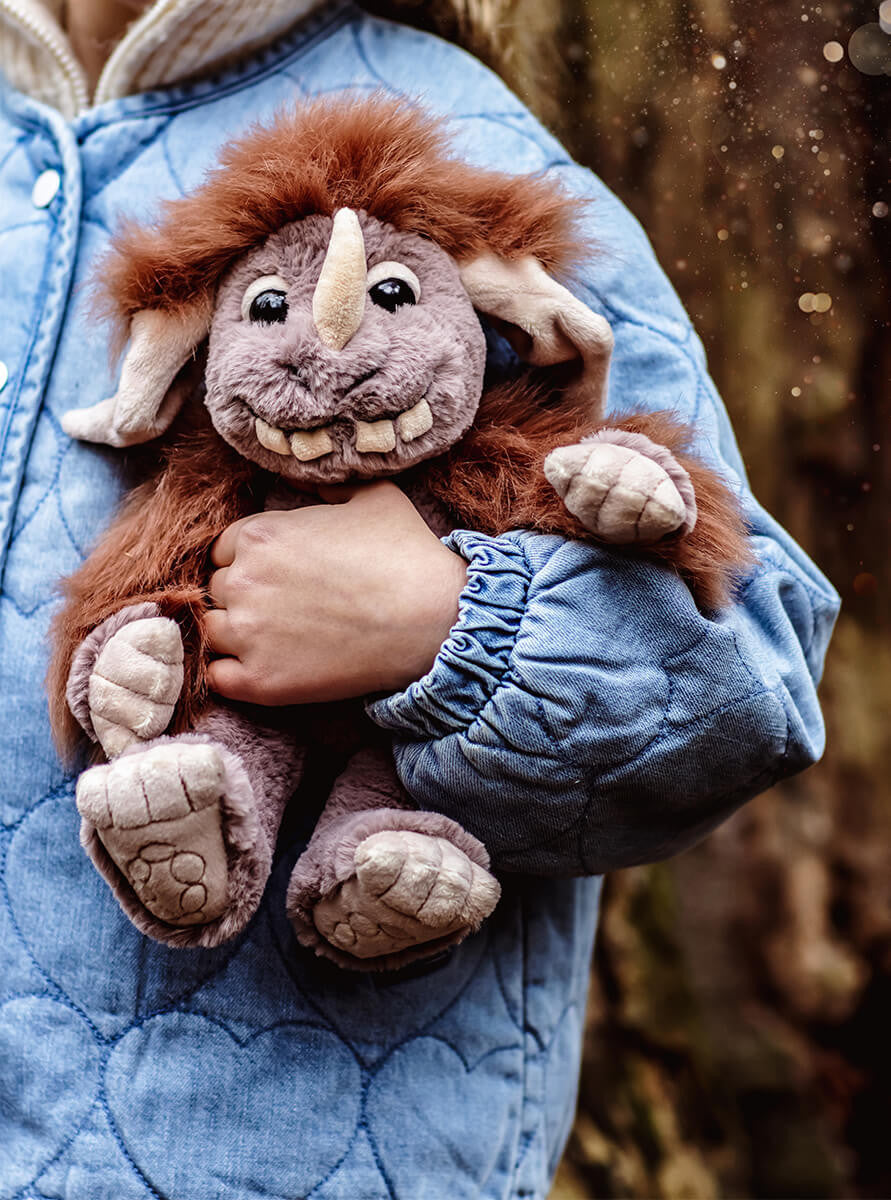 Person holding a plush toy with a fantasy design against a blurred natural background