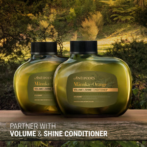 Two bottles of Antipodes Manuka & Orange Volume & Shine Conditioner on a wooden surface with a natural background.