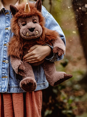 Person holding a plush toy with a unicorn and lion design in a natural setting