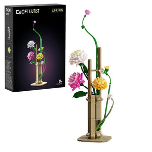 Model building kit of a flower arrangement with a black box labeled 'Cada Vez Est', on a white background.