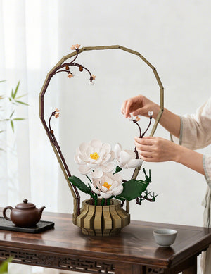 Person arranging flowers in a wooden vase on a table with a teapot and cup in the background.