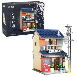 Model of a small building with a blue roof and red door, next to its packaging box.