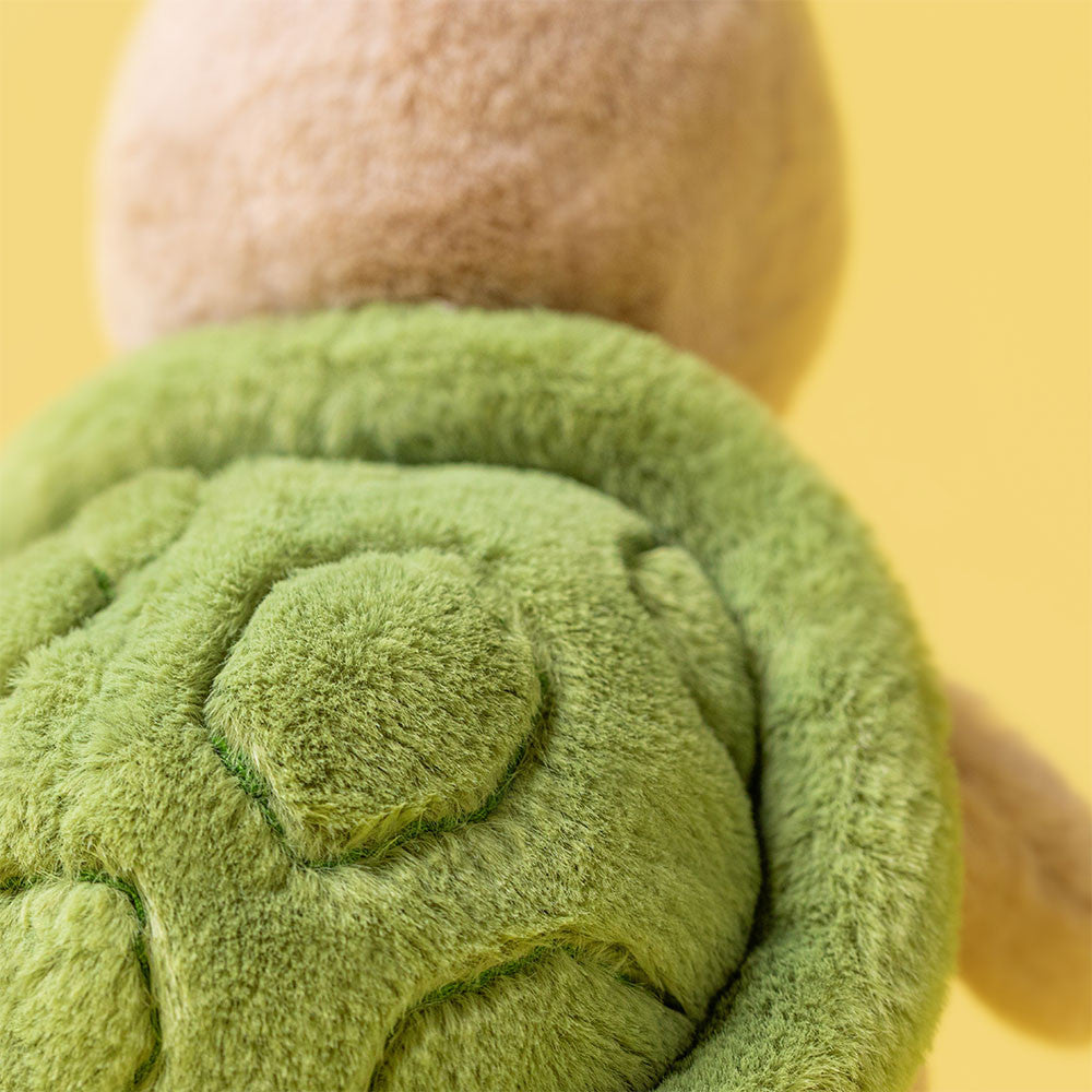 Green plush toy held by a hand against a yellow background