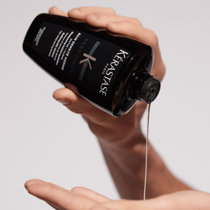 Hand pouring Kerastase product into another hand against a neutral background