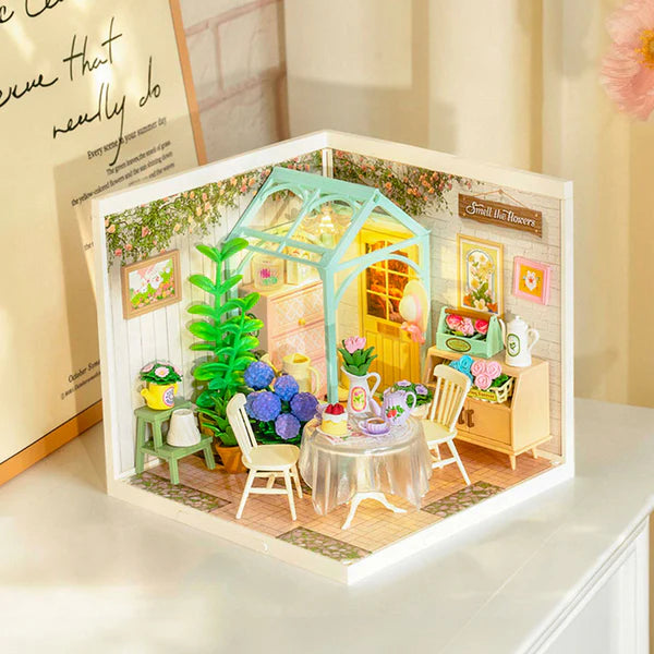Miniature model of a garden scene with a table, chairs, and plants inside a framed display.