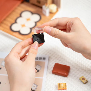 Person holding a small black camera-like device with a transparent cover on a textured surface.
