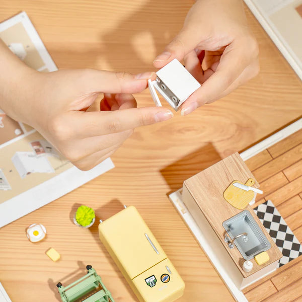 Small white sharpener being held by hands on a wooden surface with stationery items.