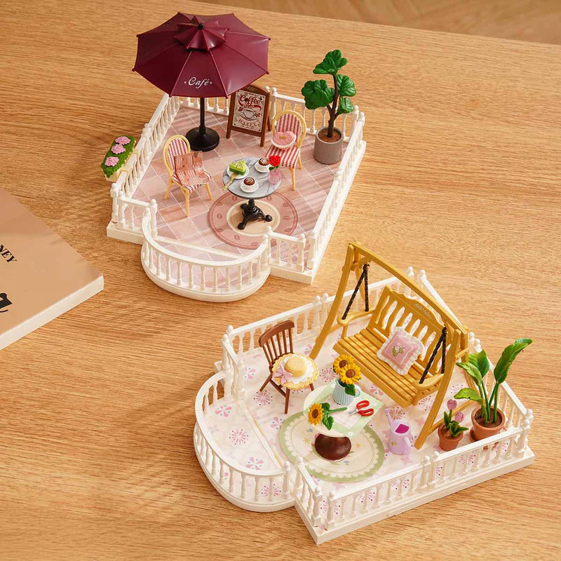 Miniature model of a patio with chairs, table, and umbrella on a wooden surface.