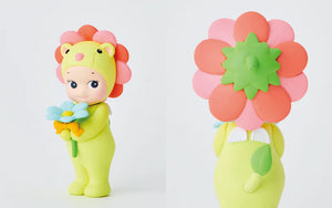 Toy figure of a lion in a green outfit holding flowers next to a toy flower with a watering can on a white background