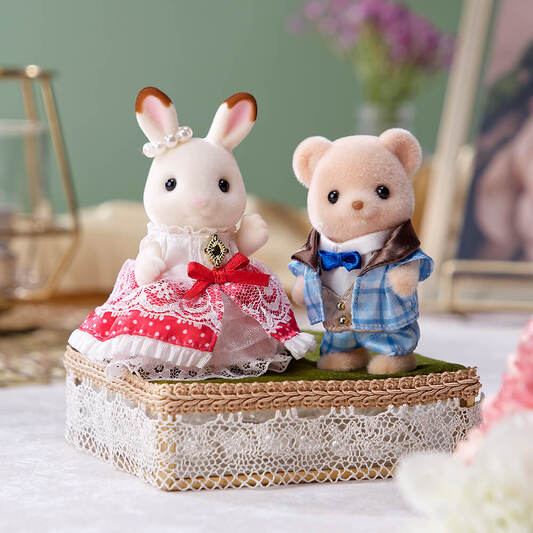 Two toy animals, a rabbit and a bear, standing on a decorative box with a blurred background.