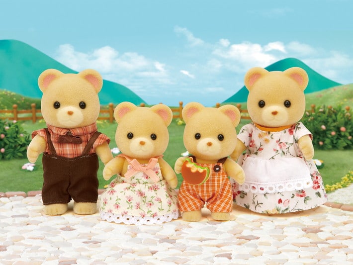 Four teddy bear toys in a scenic outdoor setting with mountains and greenery.