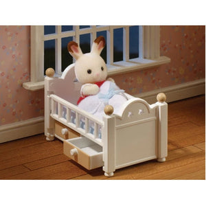 Small toy rabbit in a white crib with a blue blanket in a room with floral wallpaper.