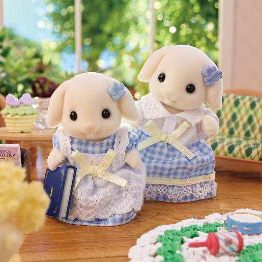 Two plush toys in blue and white dresses with decorative bows on a wooden surface.
