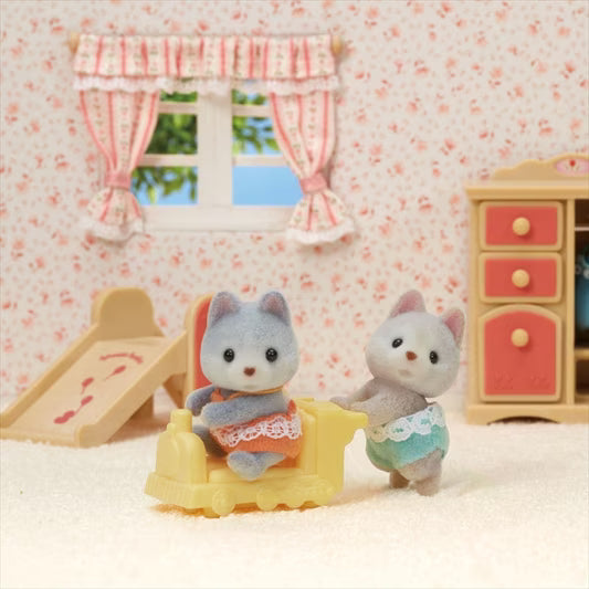 Two toy cats in a miniature room with floral wallpaper and furniture.