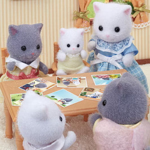 Plush toy cats sitting around a table with pictures on a decorative background
